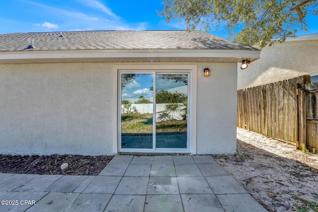 property entrance featuring a shingled roof, a patio area, fence, and stucco siding