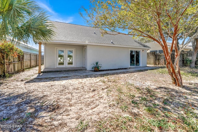 rear view of house with a patio, a fenced backyard, roof with shingles, french doors, and stucco siding