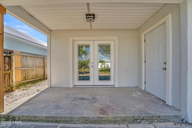 view of exterior entry featuring stucco siding, a patio area, fence, and french doors