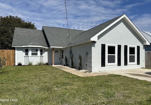 rear view of house with roof with shingles, a lawn, fence, and stucco siding