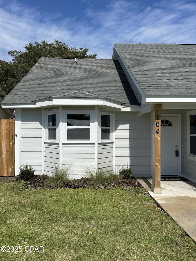 exterior space with roof with shingles, fence, and a front lawn