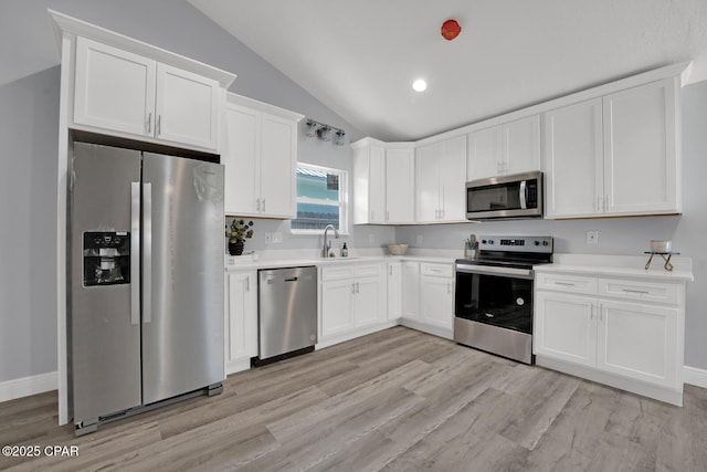 kitchen with stainless steel appliances, a sink, white cabinetry, vaulted ceiling, and light countertops