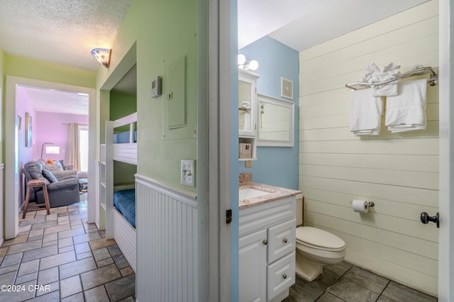 bathroom featuring vanity, toilet, a textured ceiling, and wooden walls