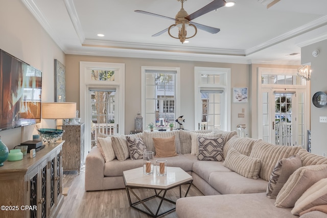 living room with light hardwood / wood-style floors, ornamental molding, a raised ceiling, and ceiling fan with notable chandelier