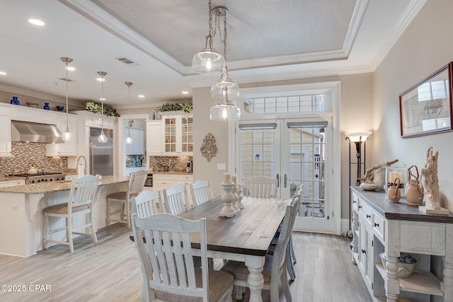 dining room featuring ornamental molding, light wood-type flooring, french doors, and a raised ceiling