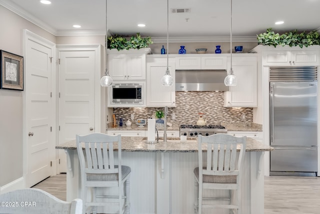 kitchen with built in appliances, range hood, light stone countertops, and white cabinetry