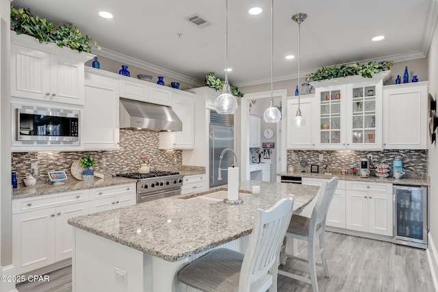 kitchen featuring built in appliances, extractor fan, decorative light fixtures, a kitchen island with sink, and sink