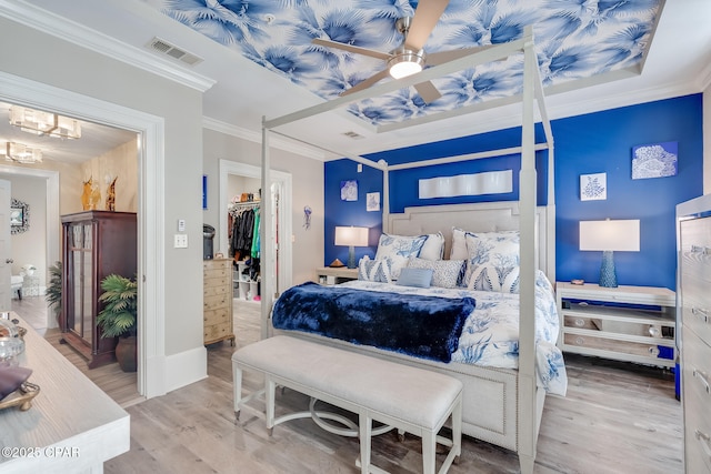 bedroom featuring a spacious closet, a closet, light wood-type flooring, ceiling fan, and ornamental molding