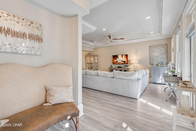 living room featuring crown molding, a raised ceiling, ceiling fan, and light hardwood / wood-style flooring