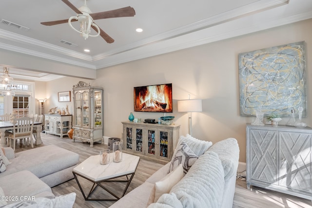 living room with ornamental molding, ceiling fan, light hardwood / wood-style floors, and a tray ceiling