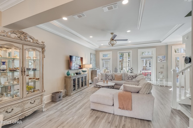 living room with crown molding, ceiling fan, light hardwood / wood-style floors, and a tray ceiling