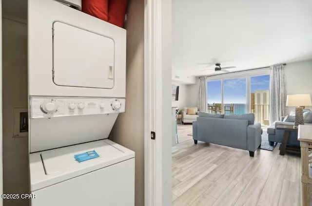 laundry area featuring ceiling fan, stacked washing maching and dryer, and light hardwood / wood-style floors