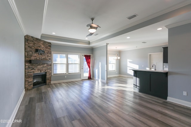 unfurnished living room featuring ornamental molding, ceiling fan with notable chandelier, a tray ceiling, dark wood-type flooring, and a fireplace