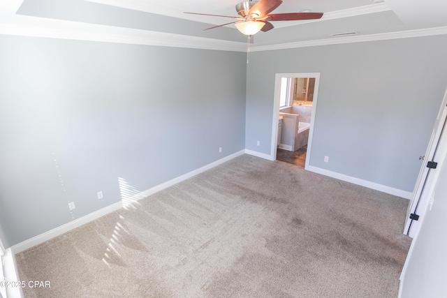 unfurnished bedroom featuring ensuite bath, carpet flooring, ceiling fan, ornamental molding, and a tray ceiling