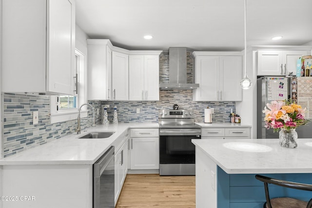 kitchen with sink, appliances with stainless steel finishes, hanging light fixtures, white cabinets, and wall chimney exhaust hood