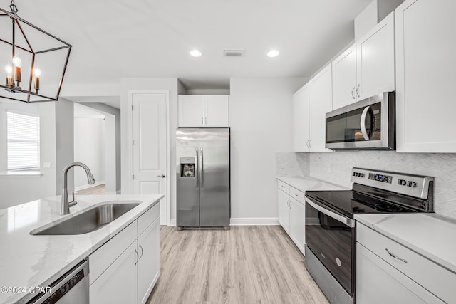 kitchen with appliances with stainless steel finishes, backsplash, sink, white cabinets, and hanging light fixtures