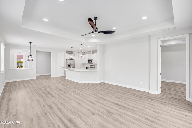 unfurnished living room with ceiling fan, light wood-type flooring, and a tray ceiling