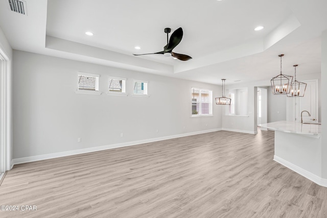 unfurnished living room with light wood-type flooring, a raised ceiling, ceiling fan, and sink