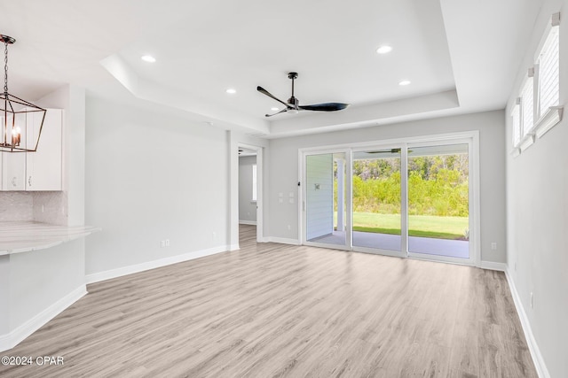 unfurnished living room featuring ceiling fan with notable chandelier, light hardwood / wood-style flooring, and a raised ceiling