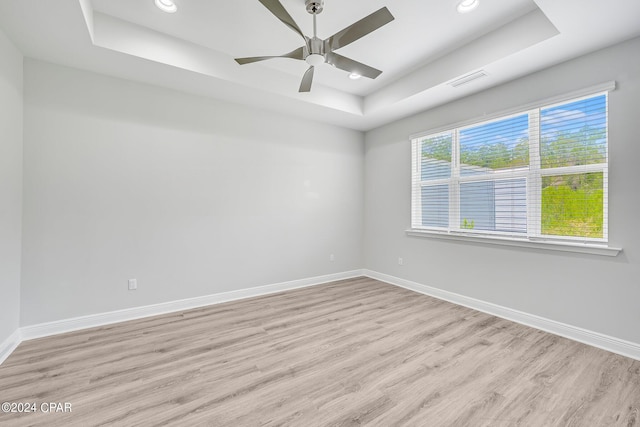 spare room featuring a tray ceiling, ceiling fan, and light hardwood / wood-style floors