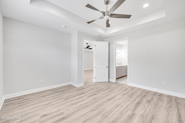 unfurnished bedroom featuring a tray ceiling, ensuite bath, ceiling fan, and light hardwood / wood-style floors