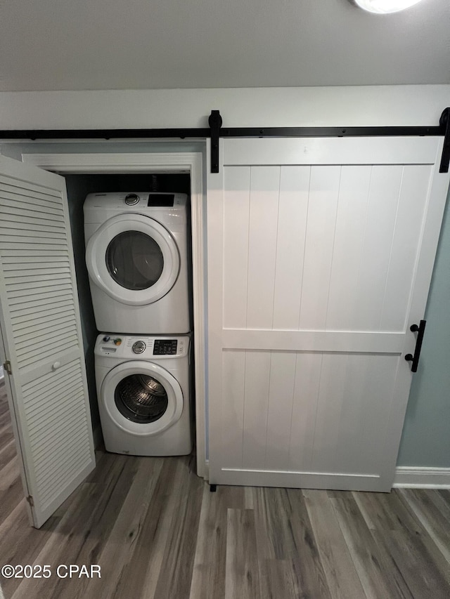 laundry area with dark hardwood / wood-style floors, a barn door, and stacked washing maching and dryer