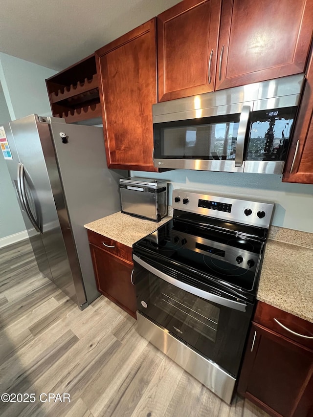 kitchen featuring appliances with stainless steel finishes, light hardwood / wood-style flooring, and light stone counters