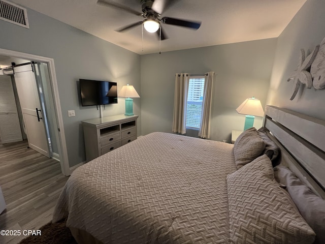 bedroom with a barn door, ceiling fan, and hardwood / wood-style flooring