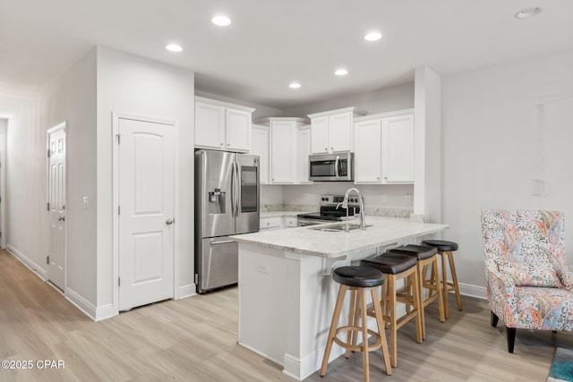 kitchen featuring sink, white cabinets, light hardwood / wood-style floors, kitchen peninsula, and stainless steel appliances