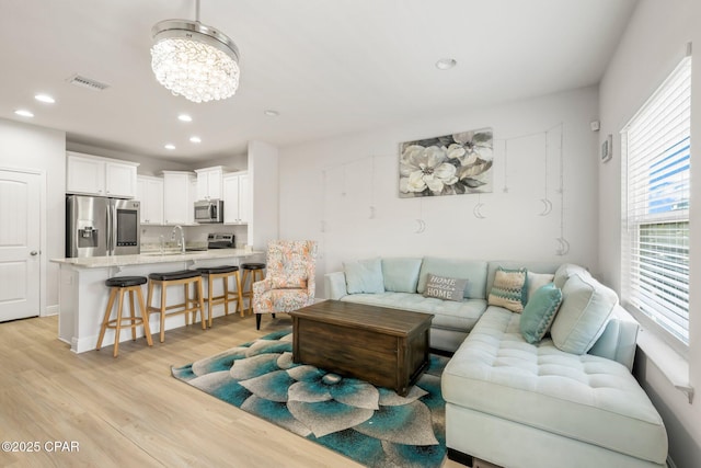 living room with an inviting chandelier, sink, and light hardwood / wood-style floors