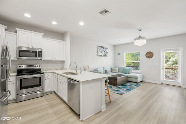 kitchen with white cabinetry, stainless steel appliances, decorative light fixtures, and sink