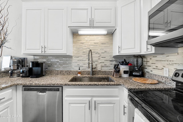 kitchen featuring decorative backsplash, white cabinets, light stone counters, appliances with stainless steel finishes, and a sink