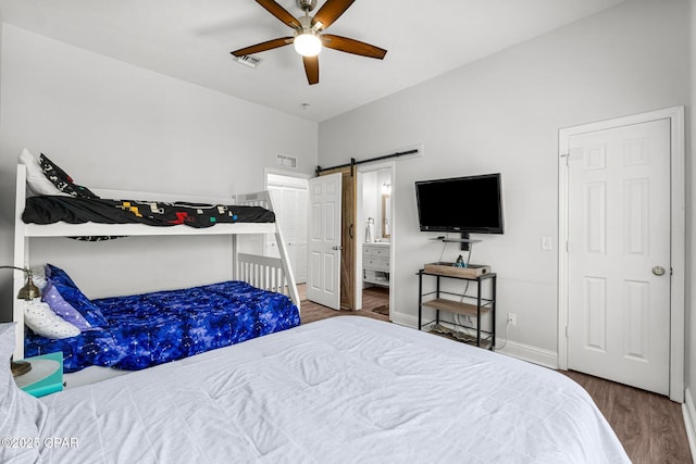 bedroom featuring wood finished floors, visible vents, baseboards, and a barn door