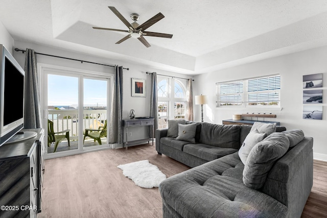 living area featuring a raised ceiling, ceiling fan, a textured ceiling, and wood finished floors