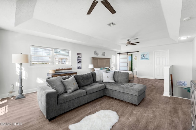 living area featuring ceiling fan, a barn door, wood finished floors, visible vents, and a tray ceiling