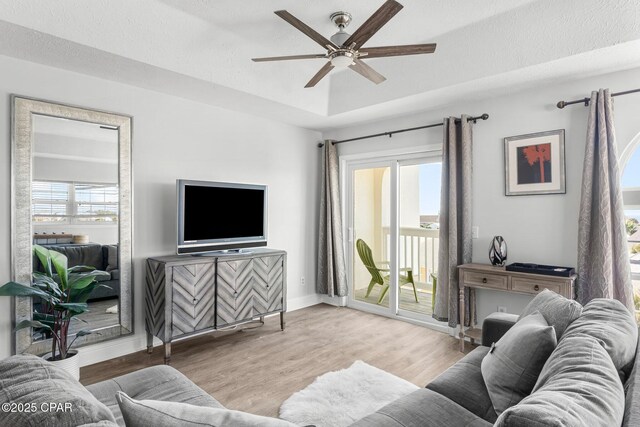 living room with a raised ceiling, ceiling fan, a textured ceiling, and light wood-type flooring