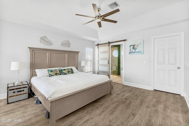 bedroom with a barn door, baseboards, visible vents, connected bathroom, and wood finished floors