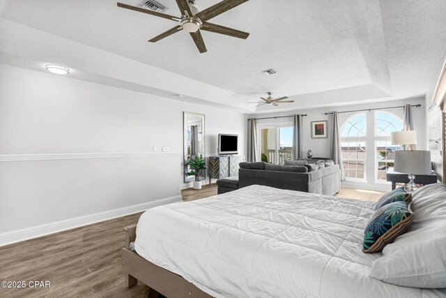 bedroom featuring a textured ceiling, a tray ceiling, ceiling fan, and hardwood / wood-style flooring