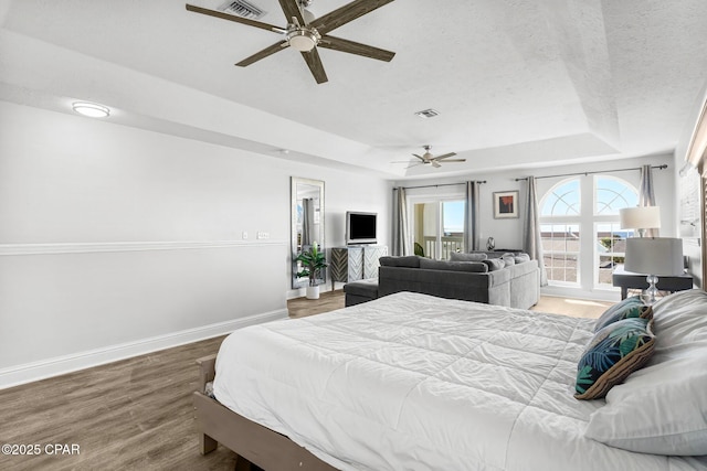 bedroom featuring visible vents, baseboards, a ceiling fan, a raised ceiling, and wood finished floors