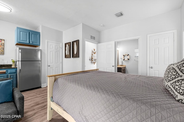 bedroom featuring visible vents, wood finished floors, freestanding refrigerator, and ensuite bathroom