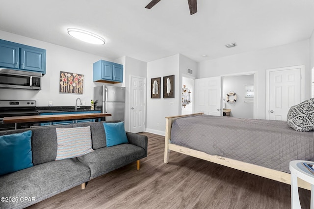 bedroom featuring freestanding refrigerator, ceiling fan, ensuite bath, wood finished floors, and baseboards