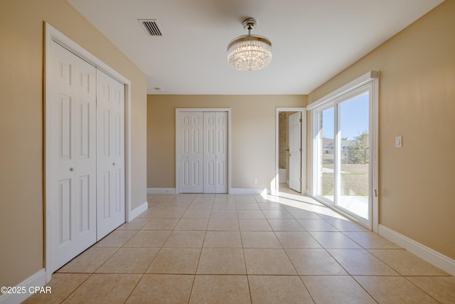 unfurnished bedroom with access to outside, a chandelier, multiple closets, and light tile patterned flooring