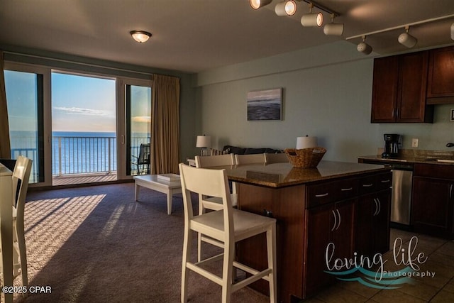 kitchen with dark carpet, dark stone counters, dark brown cabinetry, a water view, and a center island