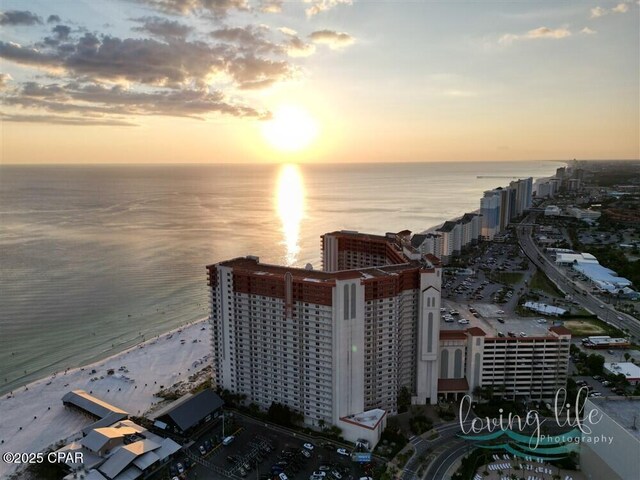 aerial view at dusk featuring a water view and a view of the beach