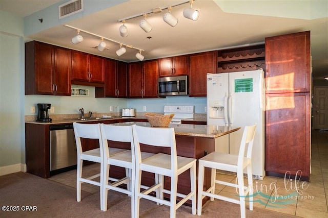 kitchen with appliances with stainless steel finishes, light stone counters, a breakfast bar, light tile patterned floors, and a center island