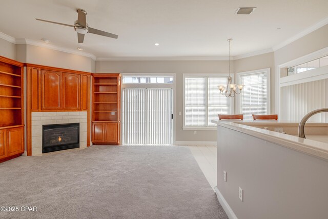 unfurnished living room featuring light carpet, crown molding, a fireplace, and ceiling fan with notable chandelier