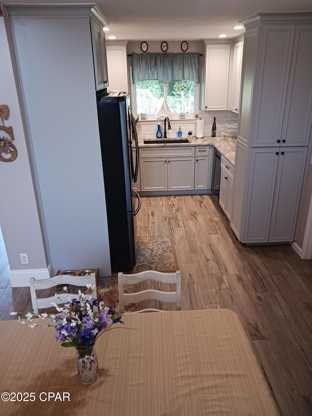 kitchen with light stone countertops, refrigerator, sink, light hardwood / wood-style flooring, and tasteful backsplash