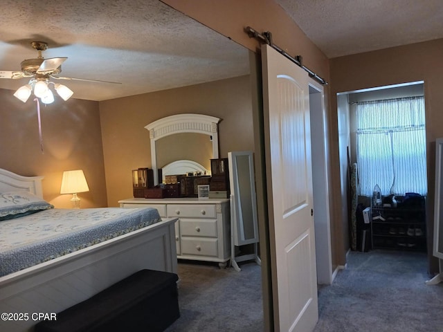 bedroom with a textured ceiling, ceiling fan, a barn door, and dark carpet