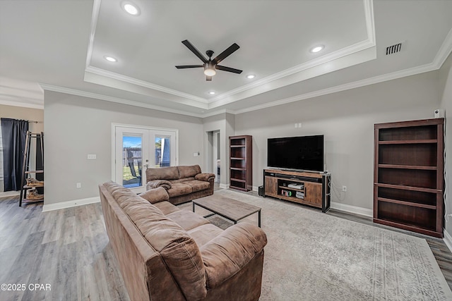 living room with ceiling fan, a raised ceiling, light hardwood / wood-style flooring, and french doors