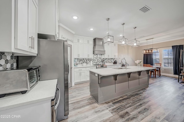 kitchen featuring custom exhaust hood, hanging light fixtures, white cabinetry, and a center island with sink